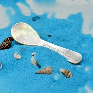 Macro shot of seashell spoon with Rosso di Mazara engraving on vibrant blue sand