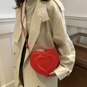 Minimalist red heart-shaped crossbody bag with gold hardware worn over a beige coat