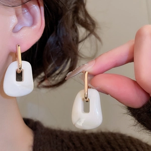 Detail of white acrylic square pendant earrings with golden geometric rectangular buckles