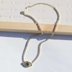 Macro detail of gold tennis chain necklace with a green zircon evil eye pendant