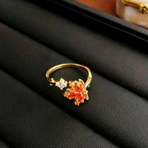 Detail of a golden open ring featuring an orange maple leaf zircon on black leather