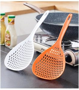 Detail of large white and orange slotted spoons with long handles in a kitchen setting