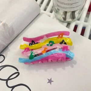 Macro detail of acrylic hair claw clip featuring colorful music notes and wavy design