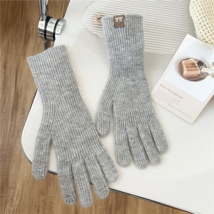 Detail of grey knitted gloves with a small brown leather brand tag on the wrist cuff