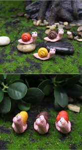 Detailed view of three mini resin snails in a micro landscape garden with green moss and pebbles