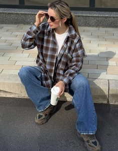 Dettaglio di una camicia a quadri marrone e blu abbinata a t-shirt bianca e jeans larghi