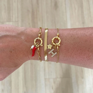 Detailed shot of layered gold bracelets featuring red chili, pearl, and star charms