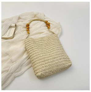 Beige straw tote bag with wooden bead handles on a white dress and open book