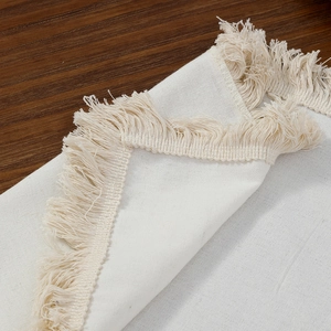 Minimalist white cotton linen place mat with elegant tassel fringe on a wooden table