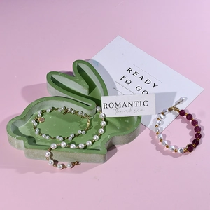 Detalle de pulseras de perlas con dijes de corazón dorado en bandeja de conejo verde