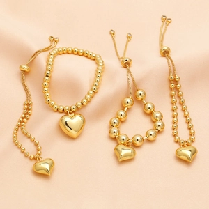 Detail of adjustable 18k gold plated bead bracelets with heart charms on pink satin