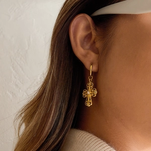 Close-up of vintage gold cross earrings with filigree design and crystals on a model