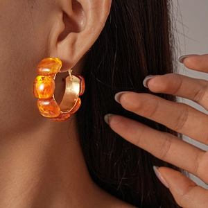 Close-up of amber resin geometric hoop earrings worn by a model in soft light