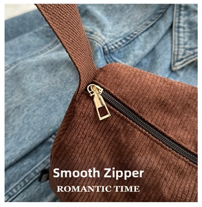 Close-up of smooth gold metal zipper on dark brown corduroy tote bag with texture