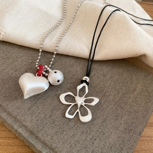 Detail of brushed silver heart and hollow flower pendants on layered metal and cord chains
