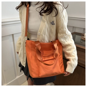 Detail of orange tote bag with adjustable shoulder strap and dual handles worn by model