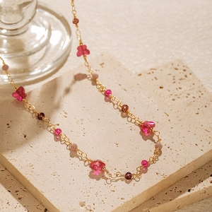 Pink butterfly bead necklace with 18K gold chain on textured stone surface