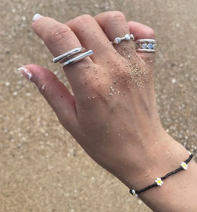 Close-up of minimalist silver rings and daisy bead bracelet on beach sand