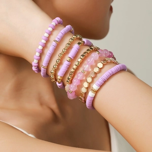 Detail of bohemian layered beaded bracelets in purple, gold and white clay beads