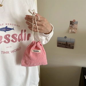 Pink drawstring storage bag with textured fabric and woven label shown held by hand
