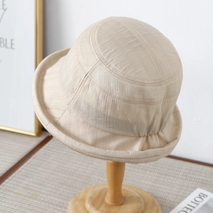 Detail view of beige bucket hat with textured fabric and rolled edge on a wooden stand
