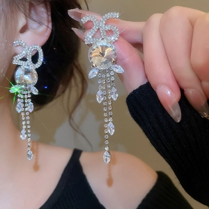 Détail macro de boucles d'oreilles chiffre 26 avec pompons et zircons sur argenté