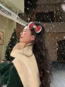 Close-up of a red velvet Christmas bow hair clip with plush trim worn by a woman outdoors