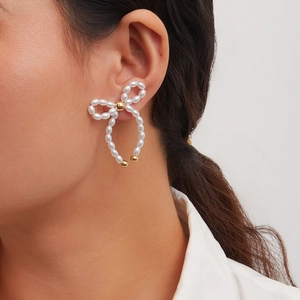 Detail of elegant bow stud earring with white pearls and gold accents on model
