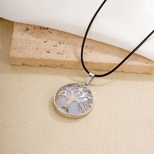 Silver tree of life pendant necklace with white opal inlay and black cord on beige stone
