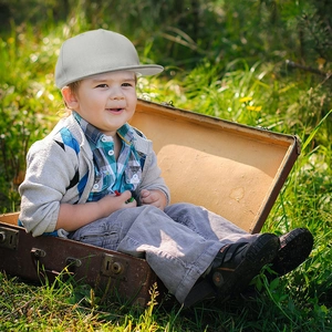 Kid boy in a grey flat brim baseball cap sitting in a vintage suitcase outdoors