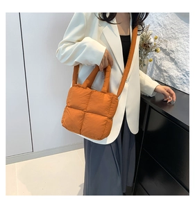 Detail of orange quilted nylon puffer bag worn as a crossbody by a fashion model