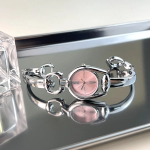 Detail of elegant silver watch with pink dial and Roman numerals on reflective surface