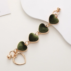 Detail view of gold metal chain bracelet with green velvet heart pendants on white backdrop