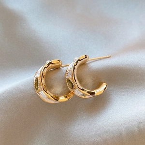 Close-up of gold-plated hoop earrings with green zircon and white enamel detail