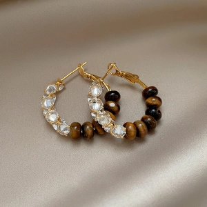 Detailed macro view of gold hoop earrings with brown tiger eye beads and zircon stones