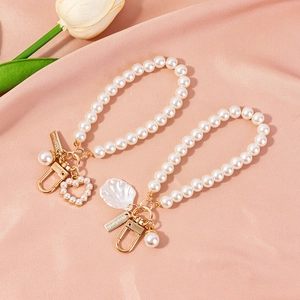 Elegant pearl keychain with gold heart charm and metallic accents on pink silk backdrop
