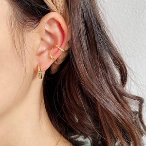 Close-up of golden textured ear cuff and hoop earring set worn on model's ear