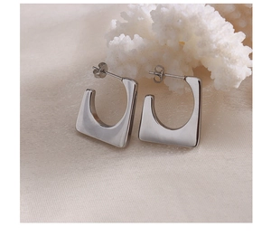 Macro detail of silver geometric trapezoid earrings on silk fabric with coral
