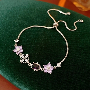 Detail of adjustable silver bracelet featuring purple flower charms and zircon pendants
