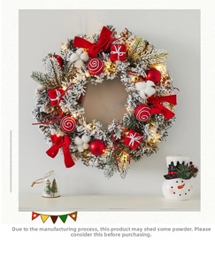 Detail of Christmas wreath with snowy pine branches, red bows and LED lights on white wall