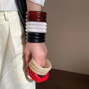 Detail of layered geometric resin bangles in amber, white and red colors on wrist