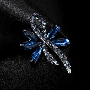 Detailed close-up of a dragonfly brooch with blue crystals and purple rhinestones on leather