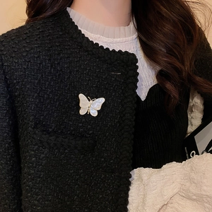 Détail d'une broche papillon fleurie avec perles sur veste en tweed noir