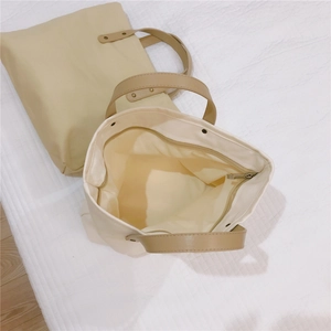Close-up of canvas tote bag featuring brown leather handles with sturdy metal rivets