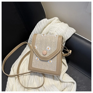 Detail of woven straw crossbody bag featuring white daisy embroidery and brown faux leather trim