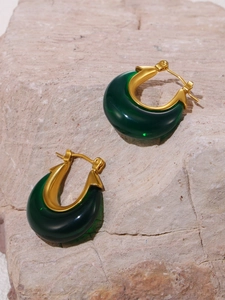 Close-up of luxury gold-plated earrings with dark green resin on a textured pink stone
