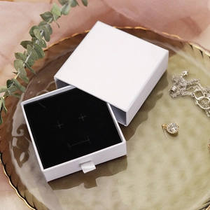 White drawer-style jewelry gift box on a gold tray with elegant ribbon handle and black insert