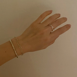 Close-up of minimalist silver cross ring and paperclip bracelet on female hand