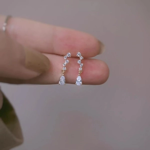 Elegant gold drop earrings with zircon crystals in pear shape shown on fingers