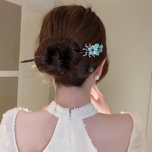 Detail view of a wooden hair stick with green flower ornament and tassel on model